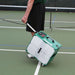 Person pulling a green and white pickleball machine on a tennis court